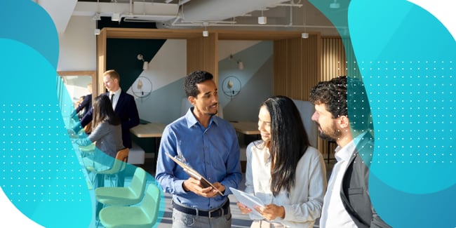 An office environment where three diverse colleagues are engaged in discussion. In the foreground, a man in a blue button-up shirt is holding documents and talking with a woman with long dark hair in a white blouse and a man with curly hair in business attire. The modern office features wooden panel accents and circular wall lights. In the background, other professionals can be seen working. The image has decorative teal curved elements and dots framing the scene, suggesting a teamwork theme.