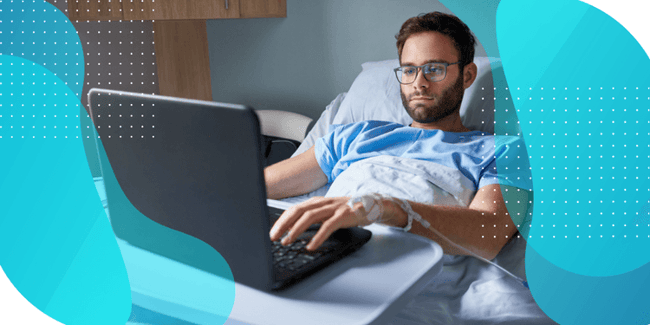 A patient in a hospital gown uses a laptop while lying in bed, researching the importance of cognitive assessments in Phase I clinical trials