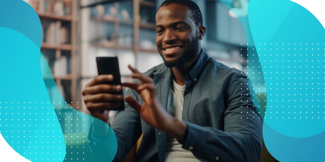 A man smiling and using his smartphone in a library-like setting, illustrating the use of eCOA software for capturing patient-reported outcomes in clinical trials.